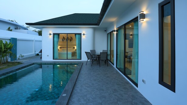 Een modern huis met een zwembad, een eethoek met stoelen en een groot raam.