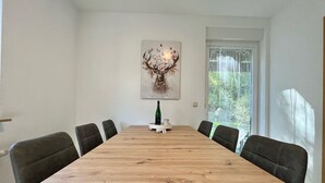 Une salle à manger avec une table en bois, six chaises, une bouteille de vin et une œuvre d’art florale accrochée au mur.