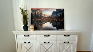 Un meuble blanc avec trois tiroirs et, au-dessus, un grand tableau représentant un paysage.