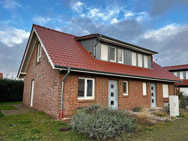 A two-story brick house with a red-tiled roof, a front door, and a small garden area.