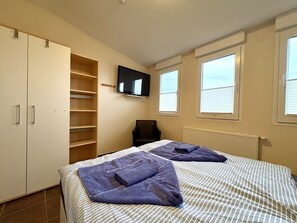 A bedroom with a bed, a TV, a chair, and a wardrobe.