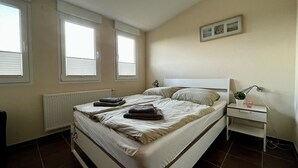Ein Schlafzimmer mit Bett, Nachttischen, einem Heizkörper und einem Fenster.