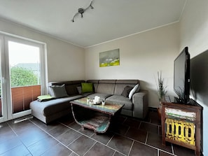 A modern living room with a sectional sofa, a coffee table, a TV, and a painting on the wall. - Holiday Home 'Haus Strandräuber Mit Sauna' with Private Terrace, Private Garden and Wi-Fi (Zierow)