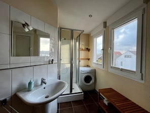 A bathroom with a sink, mirror, shower, and a washing machine.