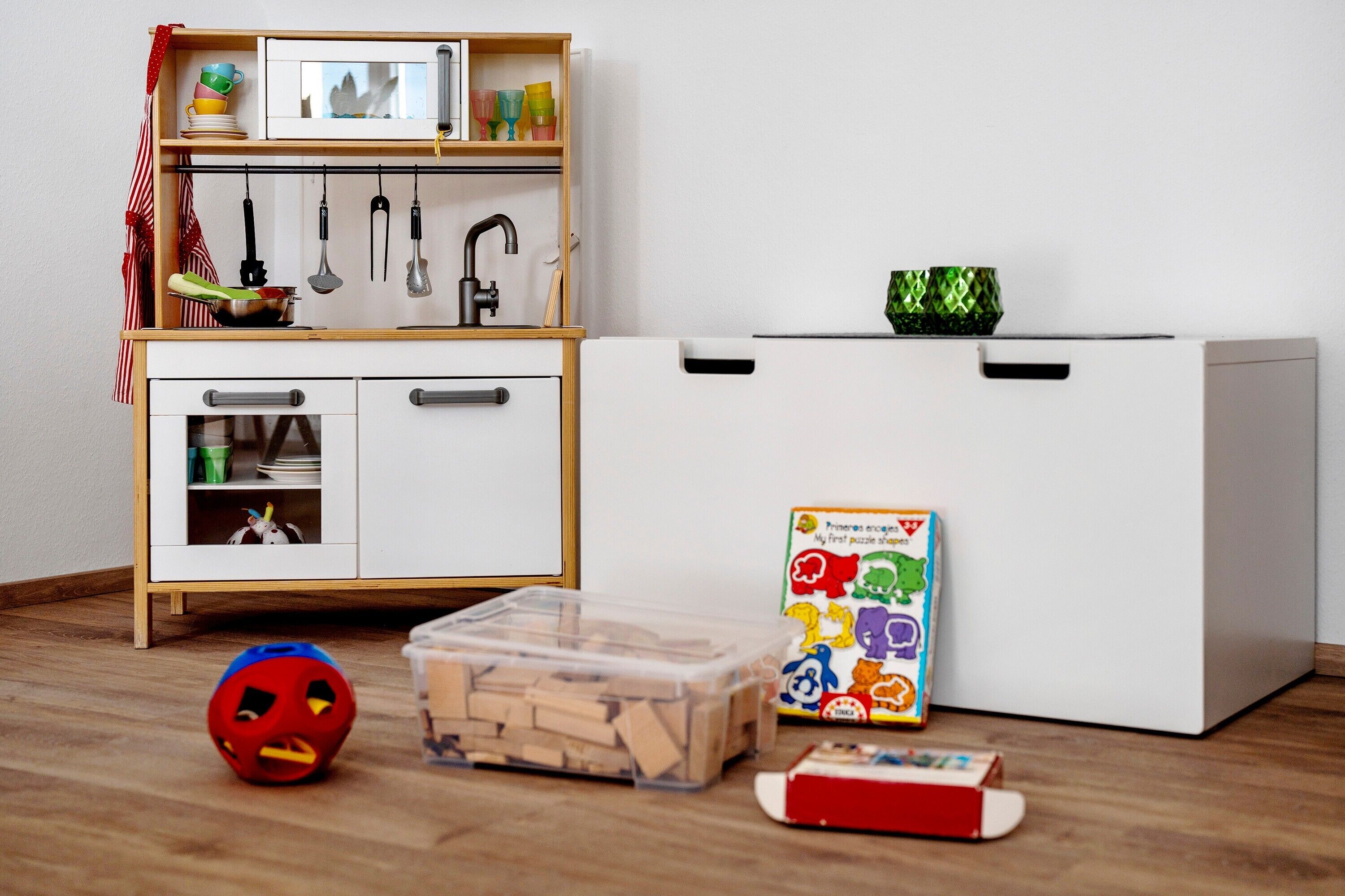 Un área de juegos infantiles con una pelota de juguete, un baúl y una caja de rompecabezas.