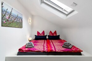 Ein Schlafzimmer mit Dachfenster, einem Bett mit gemusterten Betttextilien und einem Stadtbild an der Wand.