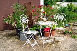 A metal outdoor table with chairs, surrounded by potted plants and flowers.