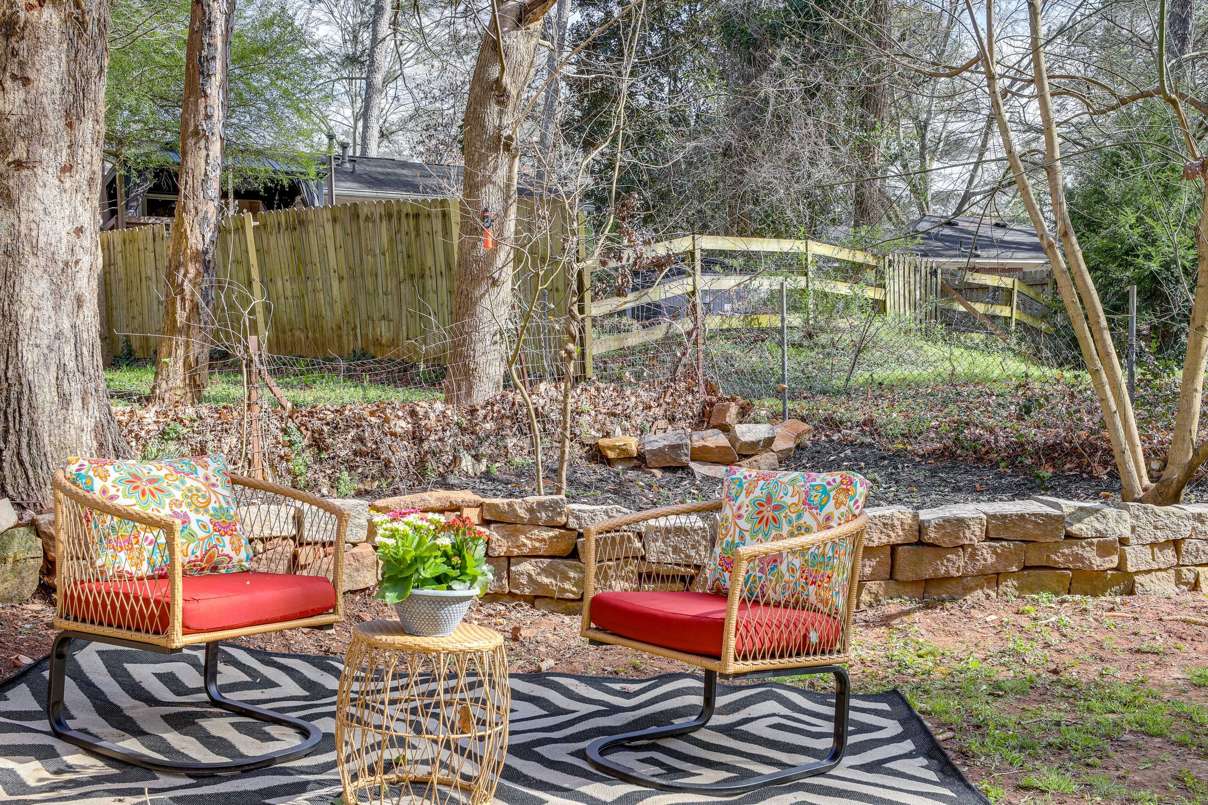 A patio area with wicker chairs and a small table, surrounded by a stone wall and a wooden fence.