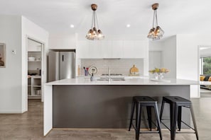 A modern kitchen with a large island, two bar stools, and pendant lighting.