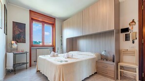A bedroom with a bed, a bedside table, a chair, a radiator, a window, and a wall-mounted heater. - Porta Di Mare Apartment With Balcony and A/C (Nardò)