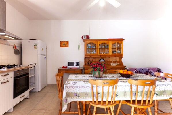 A kitchen with a stove, oven, microwave, refrigerator, wooden cabinet, dining table with chairs, and a flower vase.