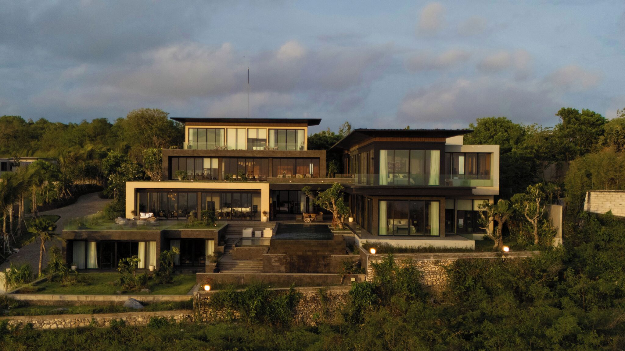 A modern multi-story house with large glass windows, a flat roof, and a well-maintained garden.