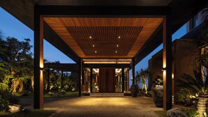 Une entrée abritée, dotée d’un plafond en bois et d’un motif en réseau, entourée de verdure et de grands jardinières.