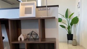 Ein modernes, mehrstufiges Holzregal mit einer Mikrowelle obenauf, einem Rauchverbotsschild und verschiedenen Dekorationselementen, darunter Bücher und Pflanzen.
