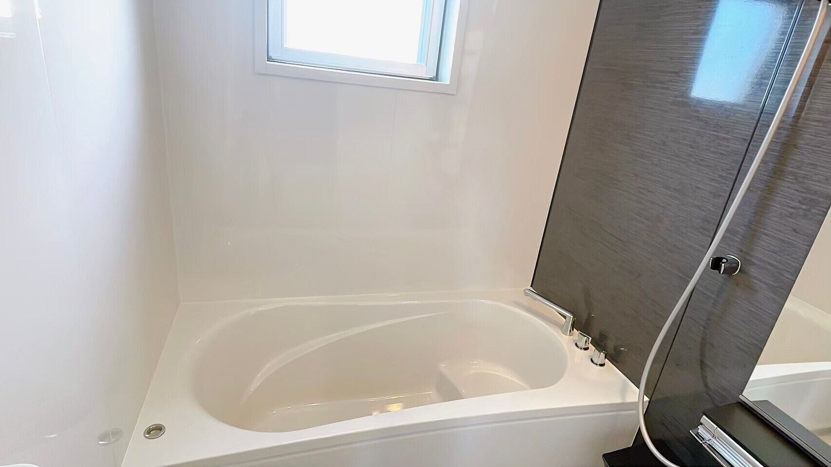 A modern bathroom with a bathtub, a window, and a shower enclosure.