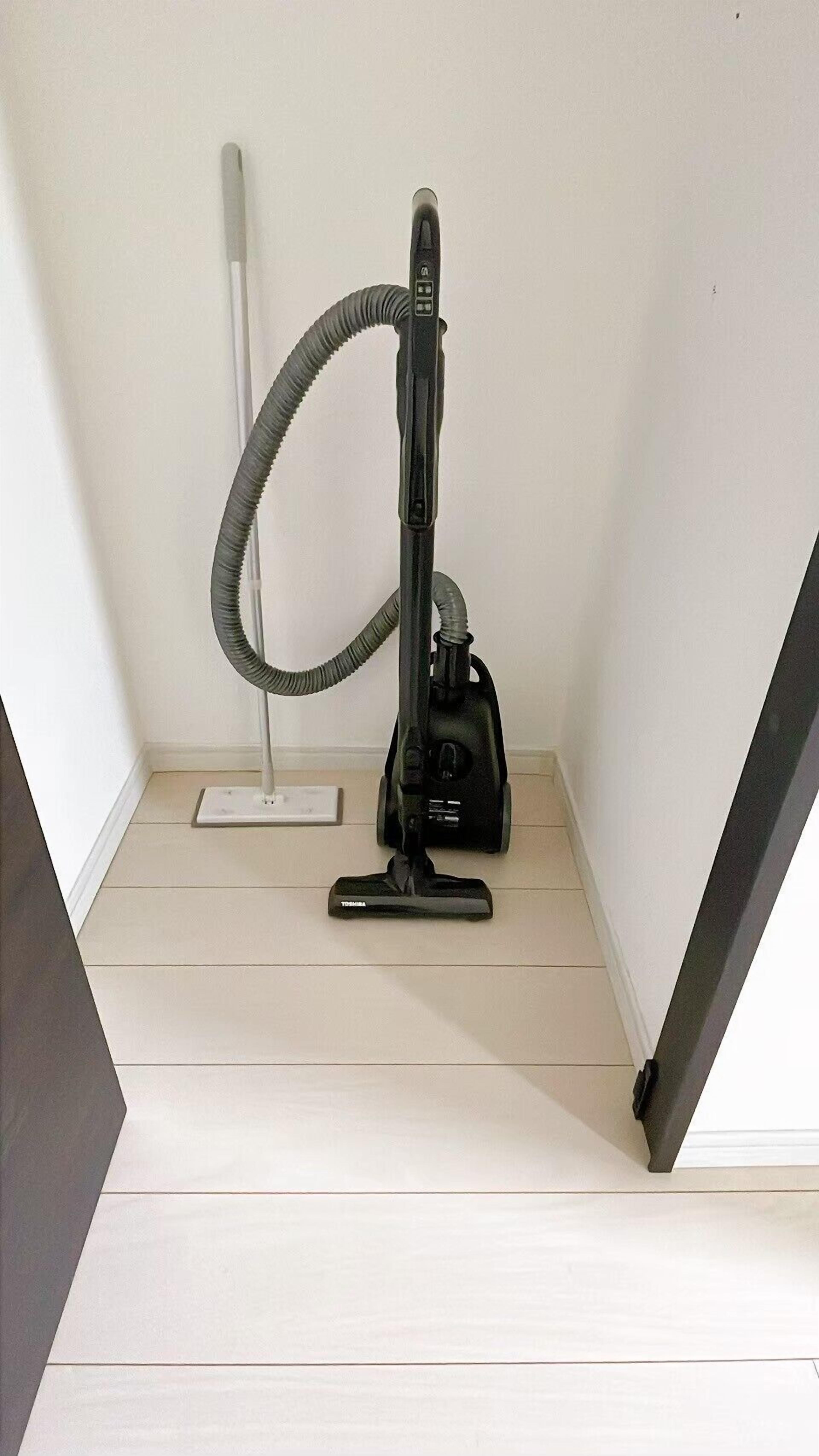 A vacuum cleaner in a corner of a room with light wooden flooring.