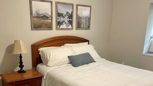 Ein Schlafzimmer mit einem hölzernen Bett, weißer Bettwäsche, einem Nachttisch mit Lampe und drei gerahmten Bildern an der Wand.
