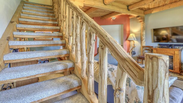 Uma escada de madeira com degraus carpetados que leva a uma sala de estar com televisão e móveis de madeira.
