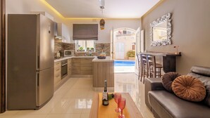 A modern kitchen with a built-in refrigerator, microwave, and stove. There is a dining area with a sofa and a table, and a view of a pool in the background. - Maisonnette & Pool Ta'cenc Sannat Gozo (Sannat)