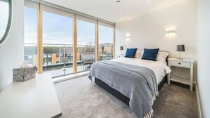 Une chambre moderne avec un grand lit, des lampes de chevet, une table de nuit et une vue sur la ville grâce à de grandes fenêtres.