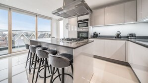 Une cuisine moderne dotée d’un îlot central, de tabourets de bar, d’appareils électroménagers en acier inoxydable et de grandes fenêtres offrant une vue sur la ville.
