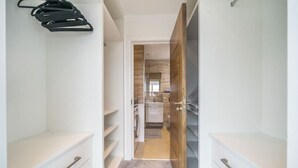 Un couloir étroit aux murs blancs, une porte en bois et une petite machine à laver visible à travers une porte entrouverte.