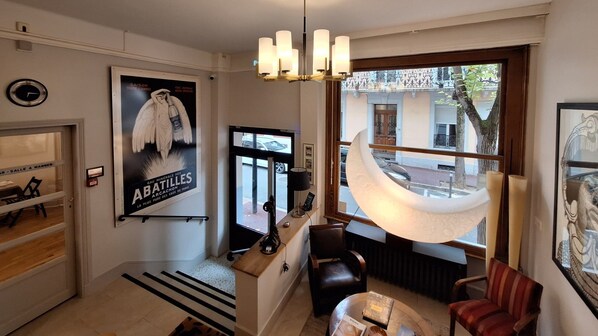 A hotel lobby with a reception desk, seating area, and a large window offering a view of the street. - Hôtel Trianon (Vichy)