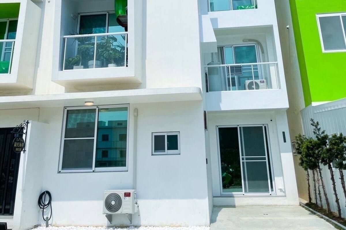 A modern multi-story building with balconies, large windows, and a green accent wall.
