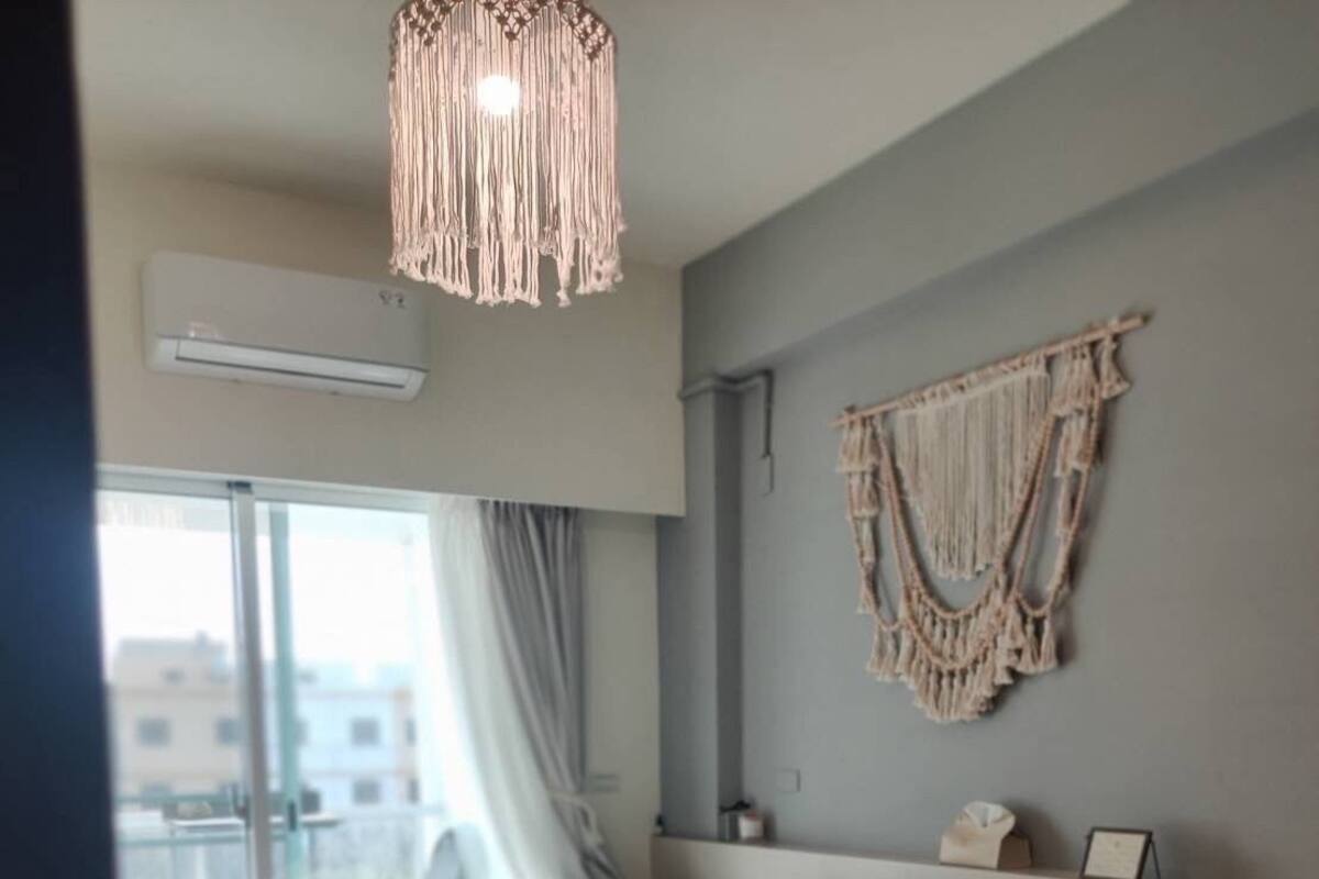A modern bedroom with a large bed, a macrame wall hanging, and a view of the city through the window.