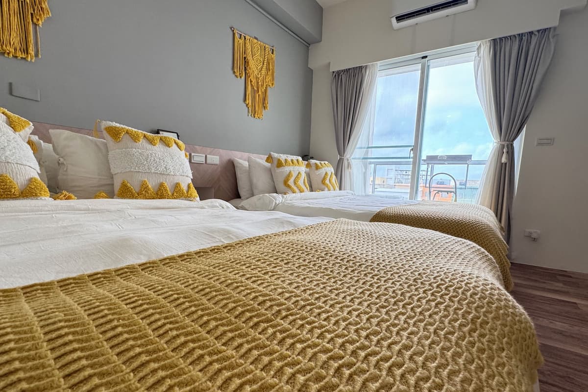 A hotel room with two beds, a large window with curtains, and a view of the city.