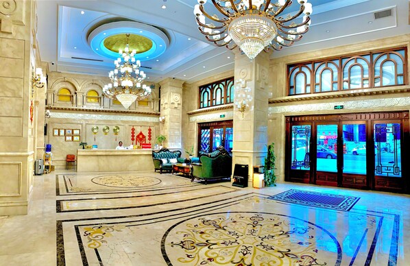 A grand lobby with a reception desk, chandeliers, and a large, ornate floor design.