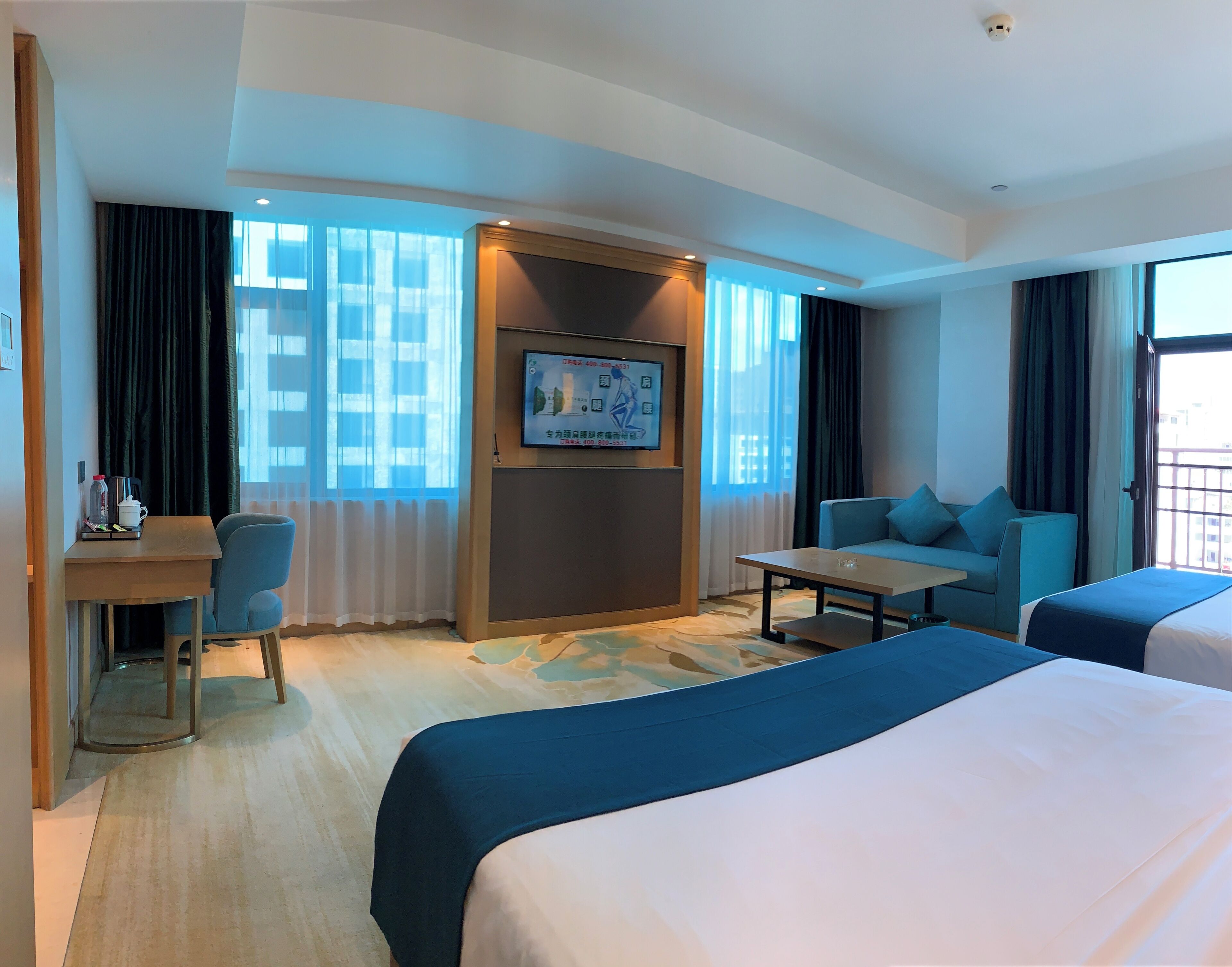A hotel room with a bed, a sofa, a desk with a chair, a TV, and a window with curtains.