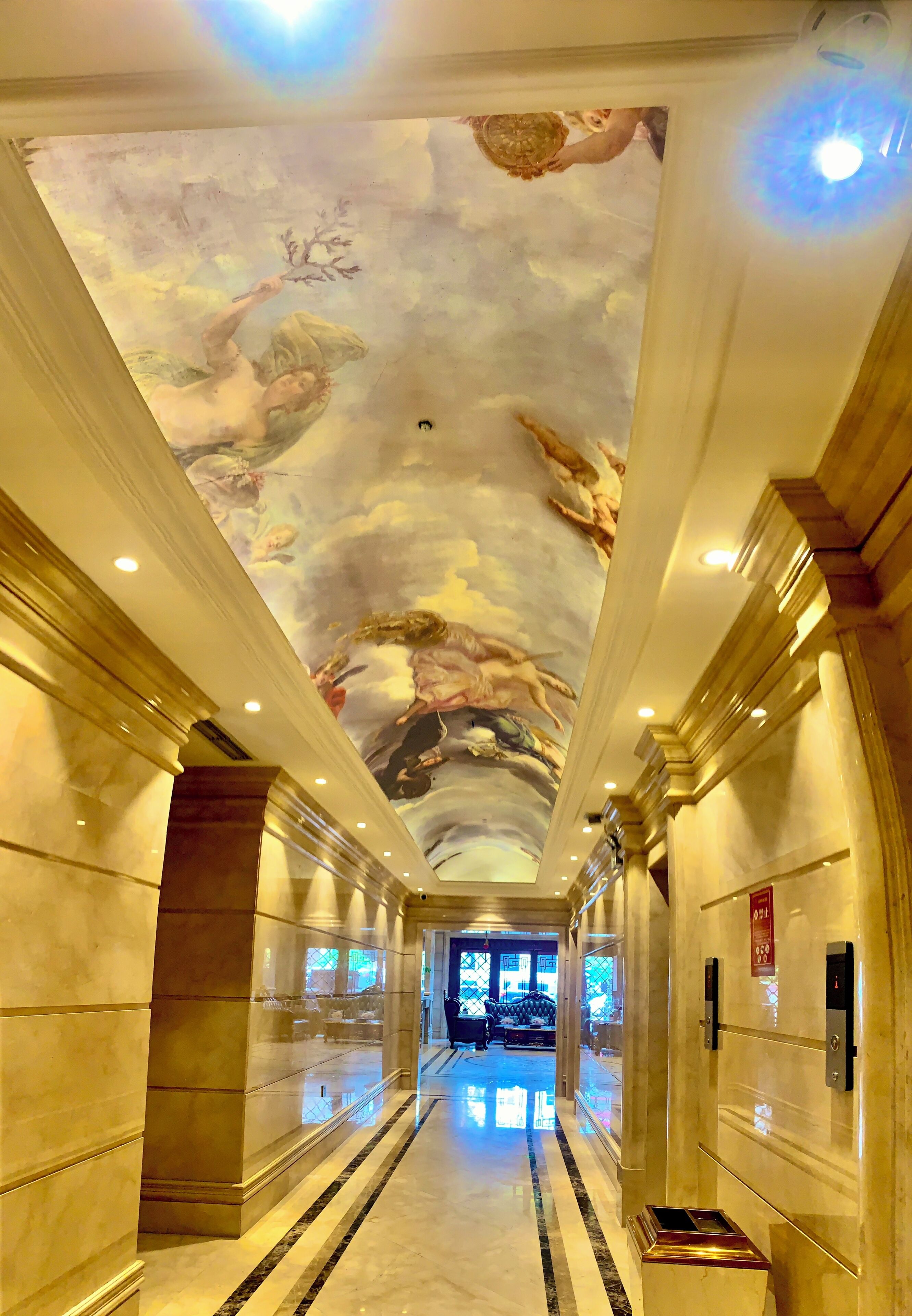Um corredor com chão de mármore e um mural no teto.