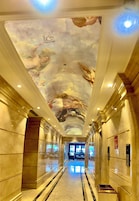 Um corredor com chão de mármore e um mural no teto.