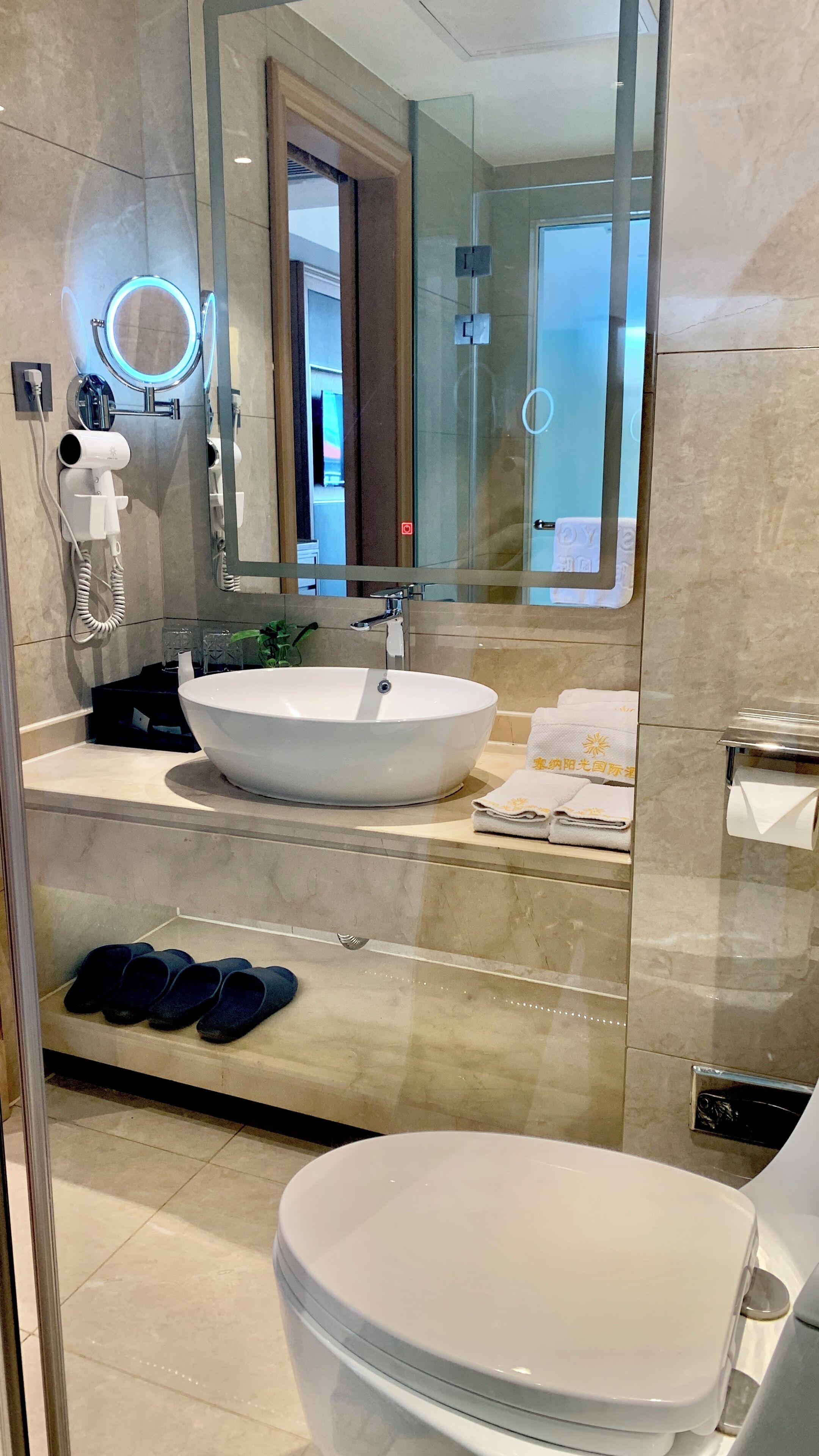 Un baño moderno con un espejo grande, un tocador redondo, un lavamanos y un inodoro.