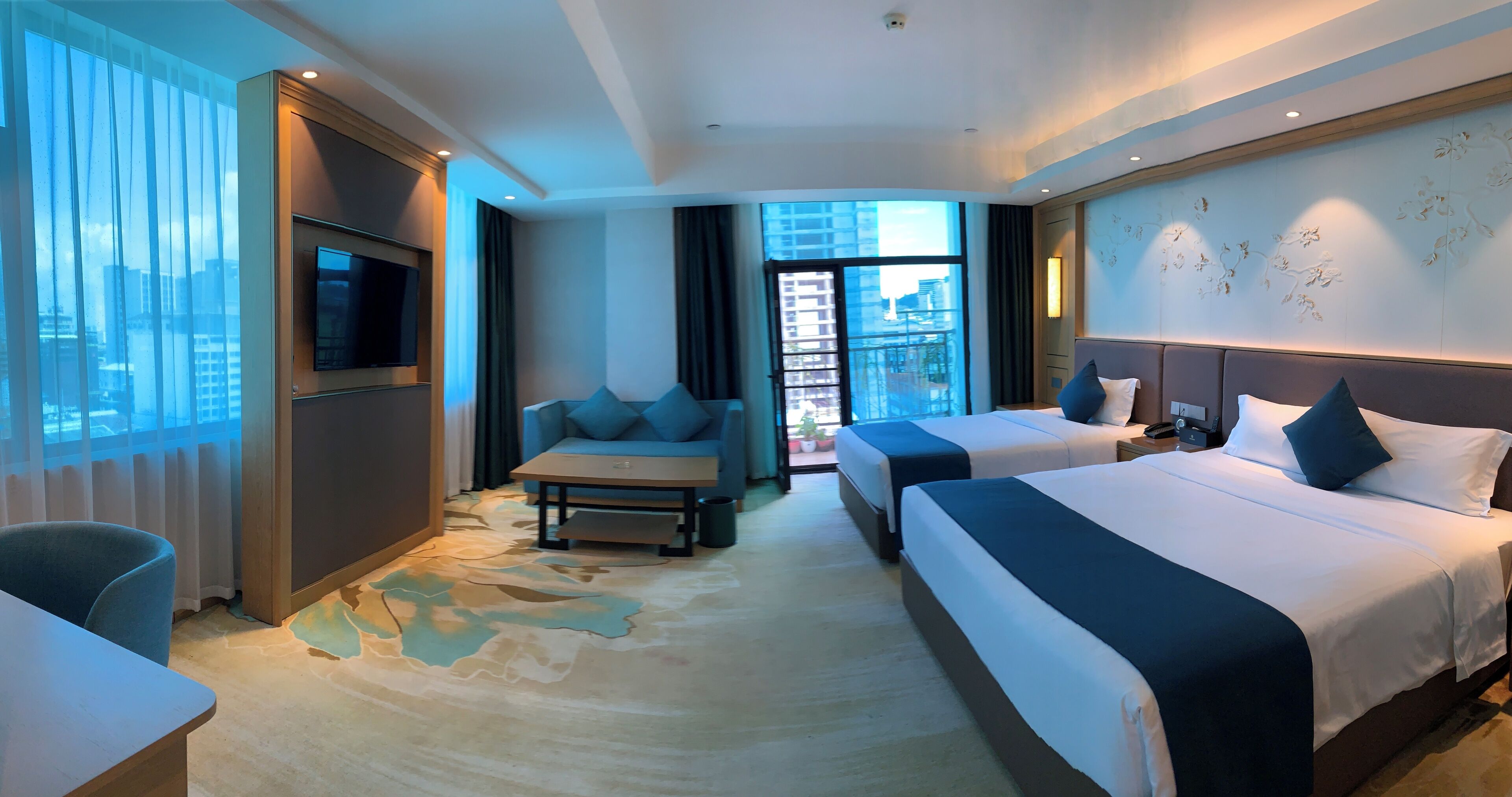 Quarto de hotel com uma cama grande, um sofá, uma televisão e uma varanda com vista para a cidade.