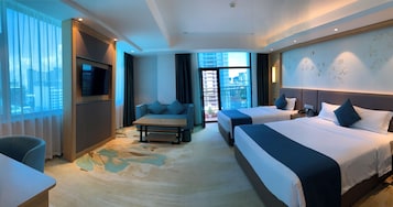 Quarto de hotel com uma cama grande, um sofá, uma televisão e uma varanda com vista para a cidade.