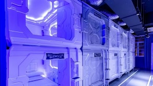 Een futuristische kamer met een centraal bed en meerdere stapelbedden, elk met een klein tafeltje en een stoel.