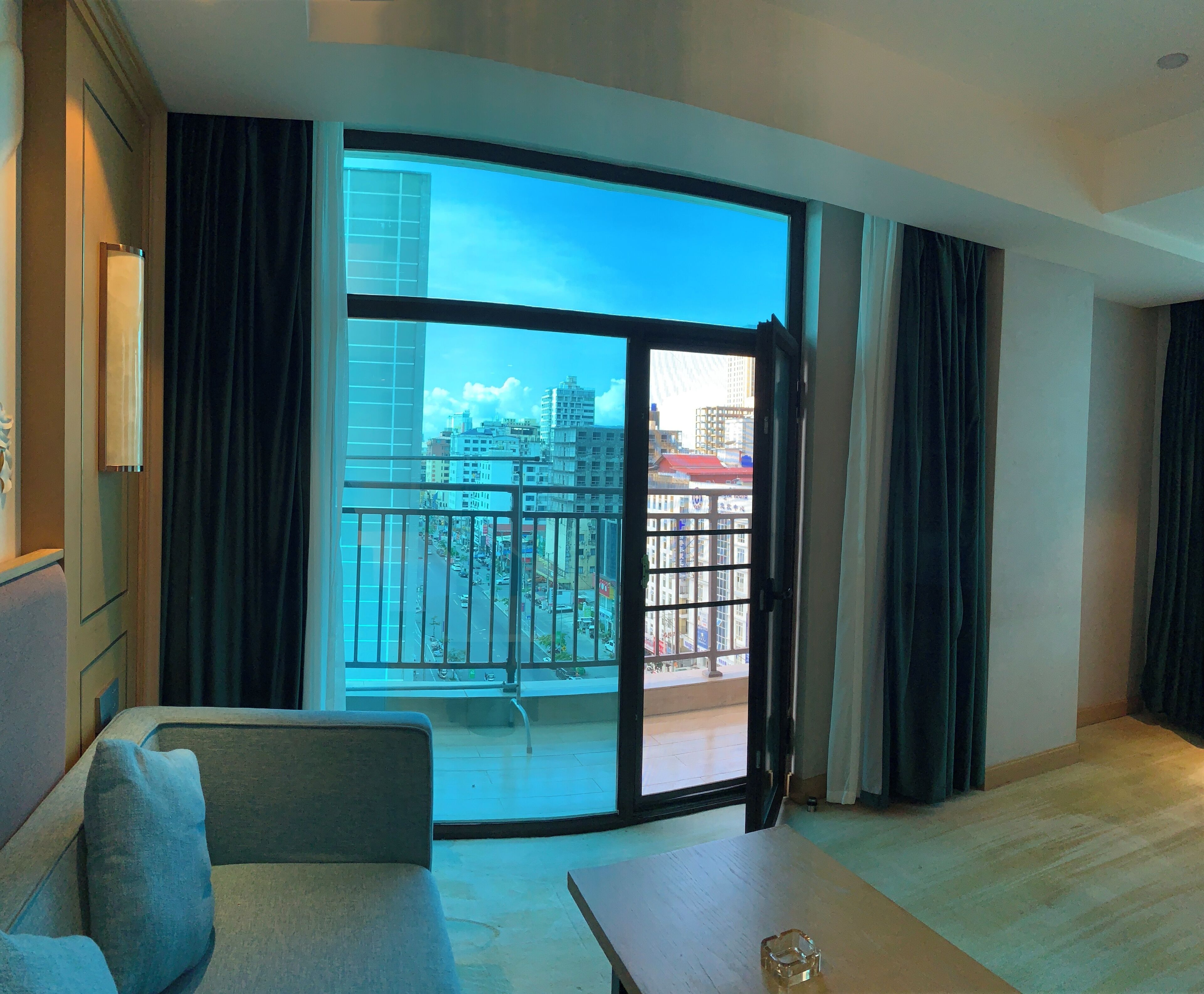 Quarto de hotel moderno com uma grande porta de vidro deslizante que dá para uma varanda, um sofá e uma pequena mesa.