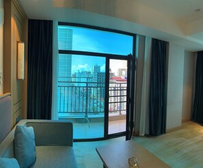 A modern hotel room with a large sliding glass door leading to a balcony, a sofa, and a small table.