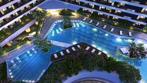 A modern hotel with a large indoor swimming pool, multiple balconies, and lush landscaping.