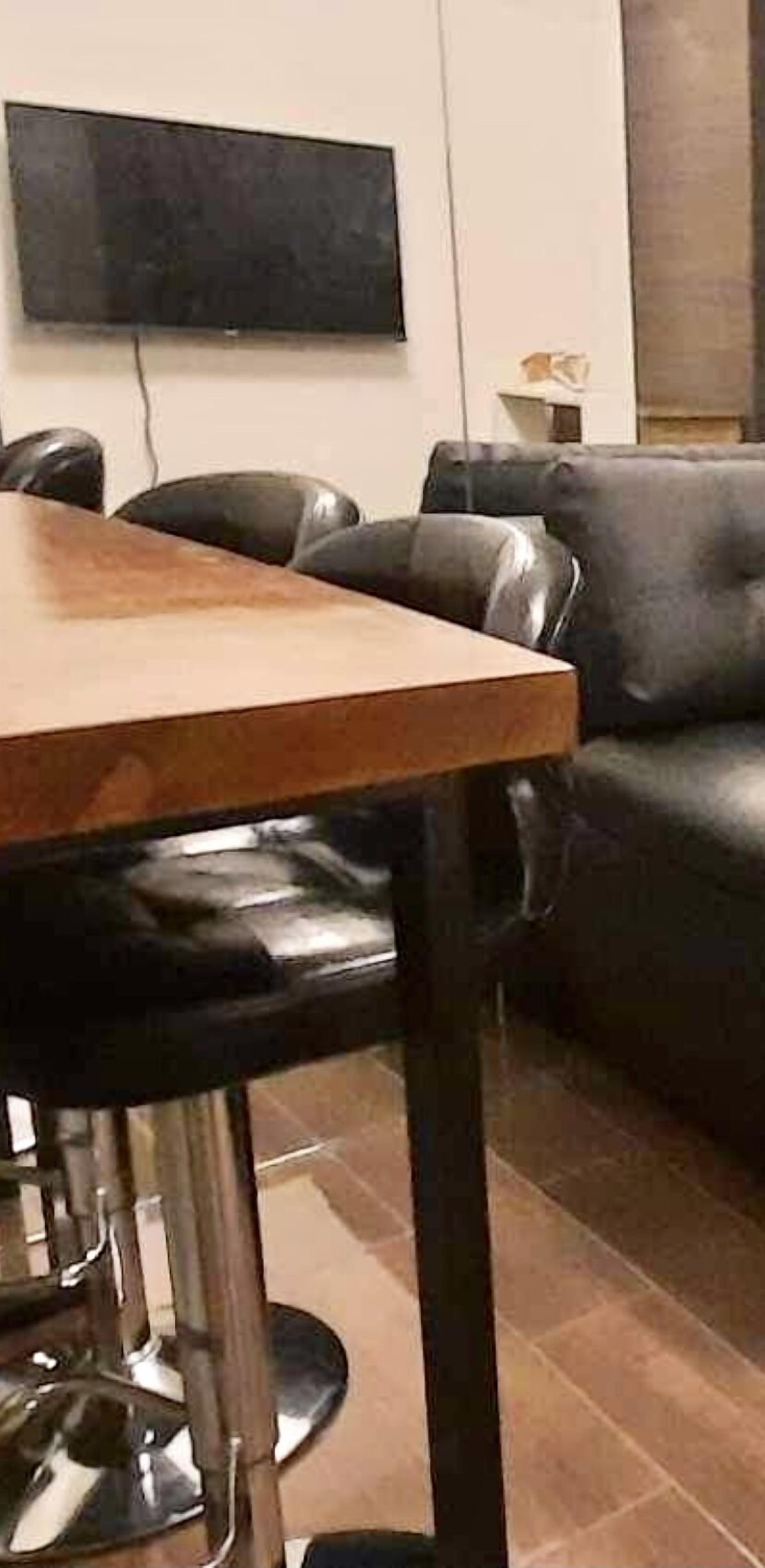 Un comedor con una mesa de madera y sillas de cuero negro. Un televisor de pantalla plana está montado en la pared sobre la mesa.