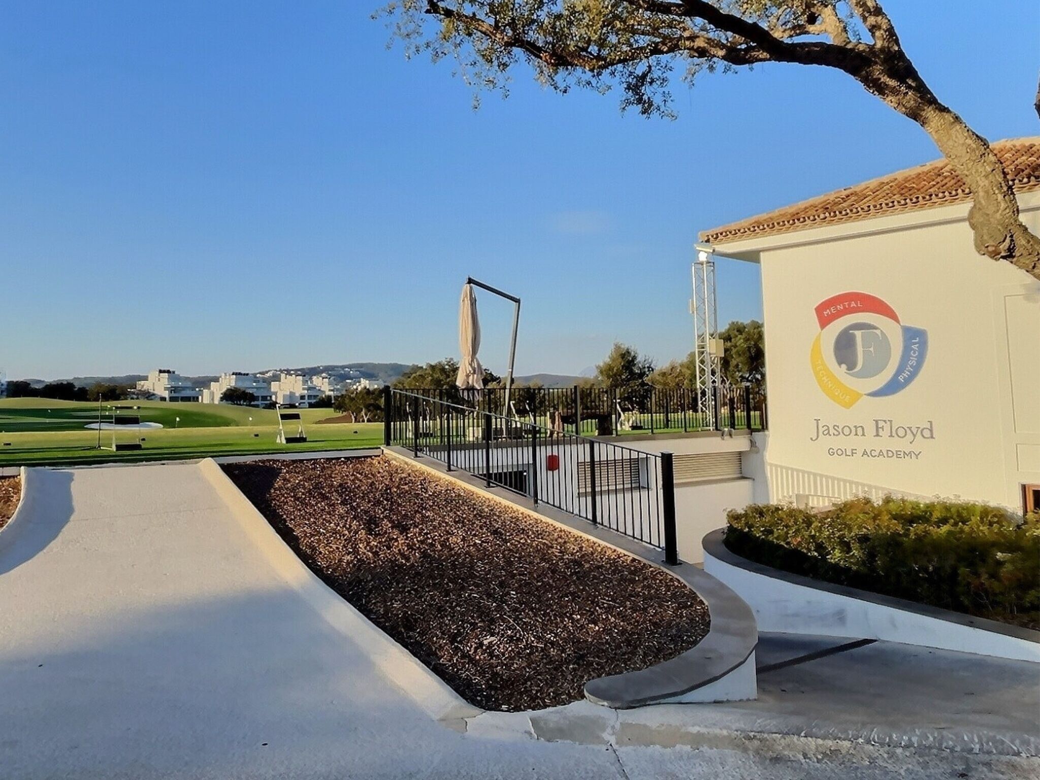 Ein Golfplatz mit einem weißen Gebäude im Hintergrund, auf dem 'Jason Floyd Golf Academy' steht.
