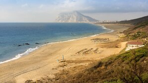 Eine Küstenlandschaft mit Strand, einem Berg im Hintergrund und einigen Gebäuden am Ufer.