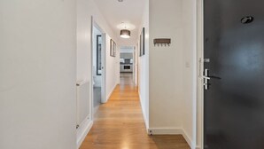 A hallway with wooden flooring, white walls, and a dark door.