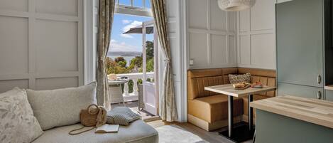 A room with a sofa, a small table, a bench, a hanging light fixture, and a view through a window.