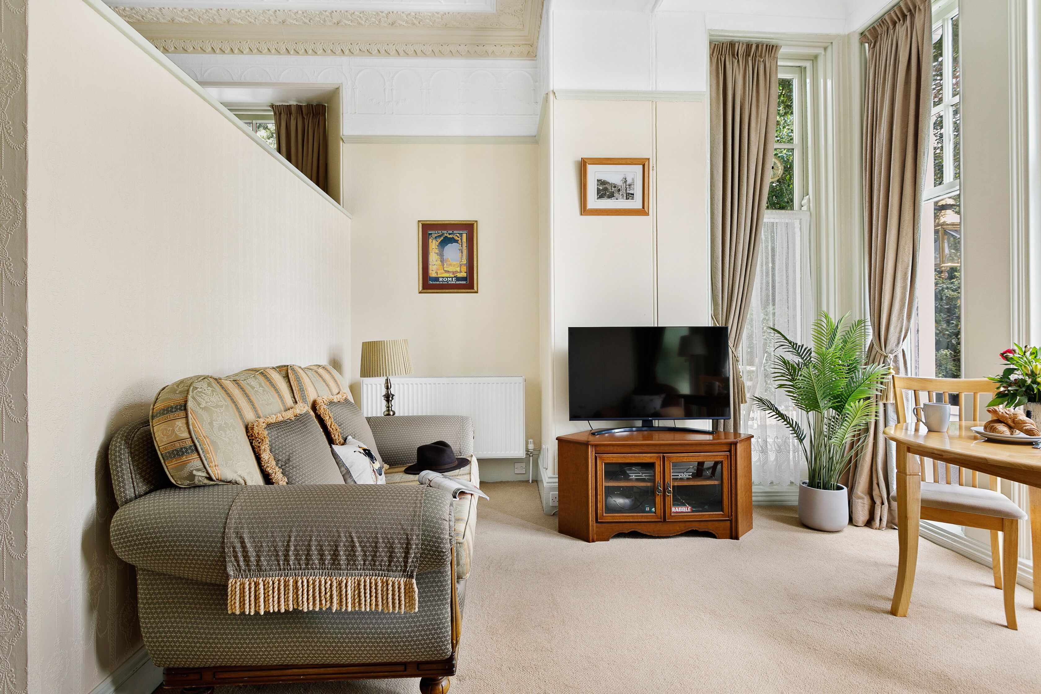 A living room with a sofa, television, wooden cabinet, dining table, and potted plant.