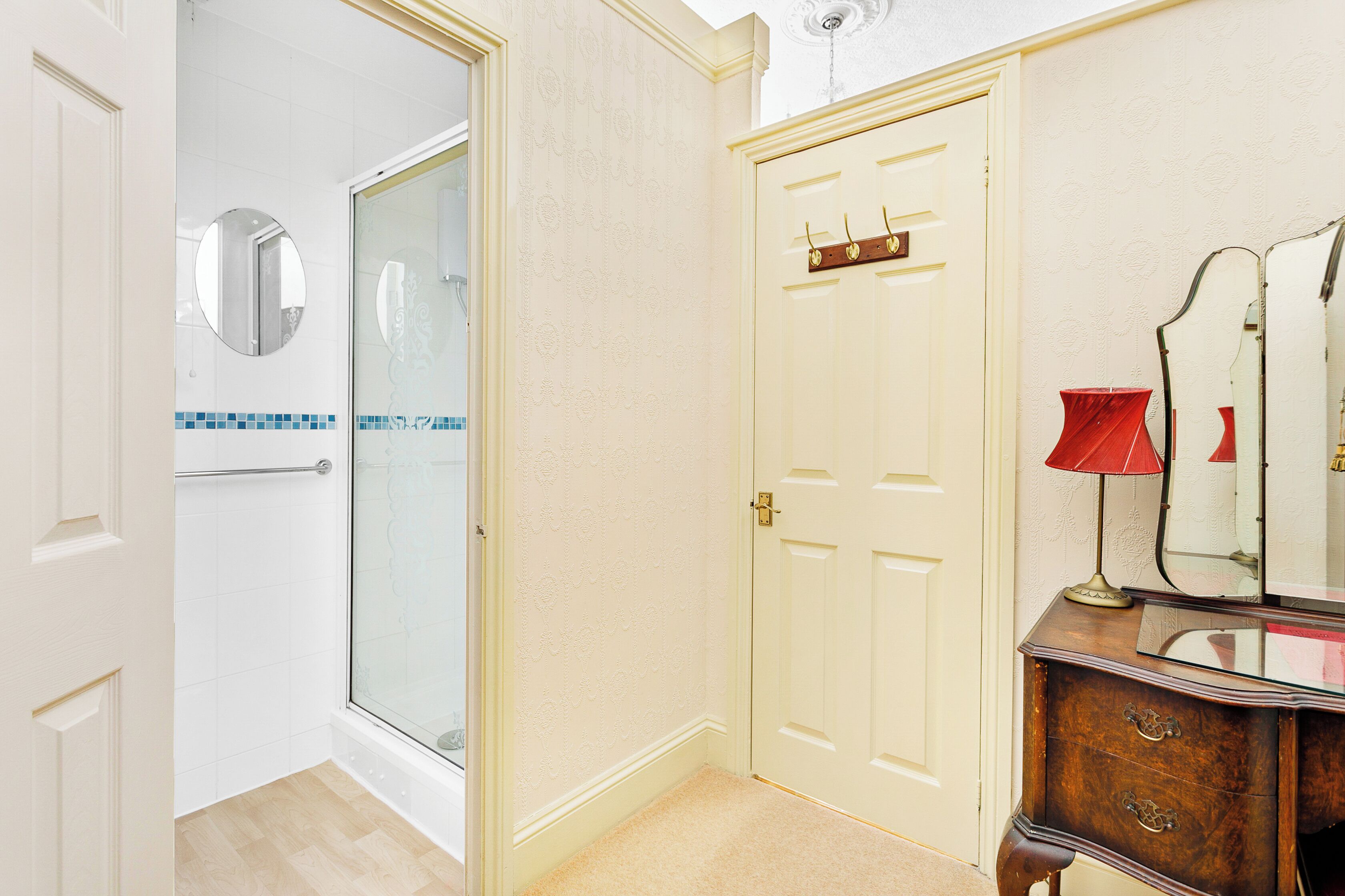 A bathroom with a glass shower, a white door, a vanity with a mirror, and a red lamp.