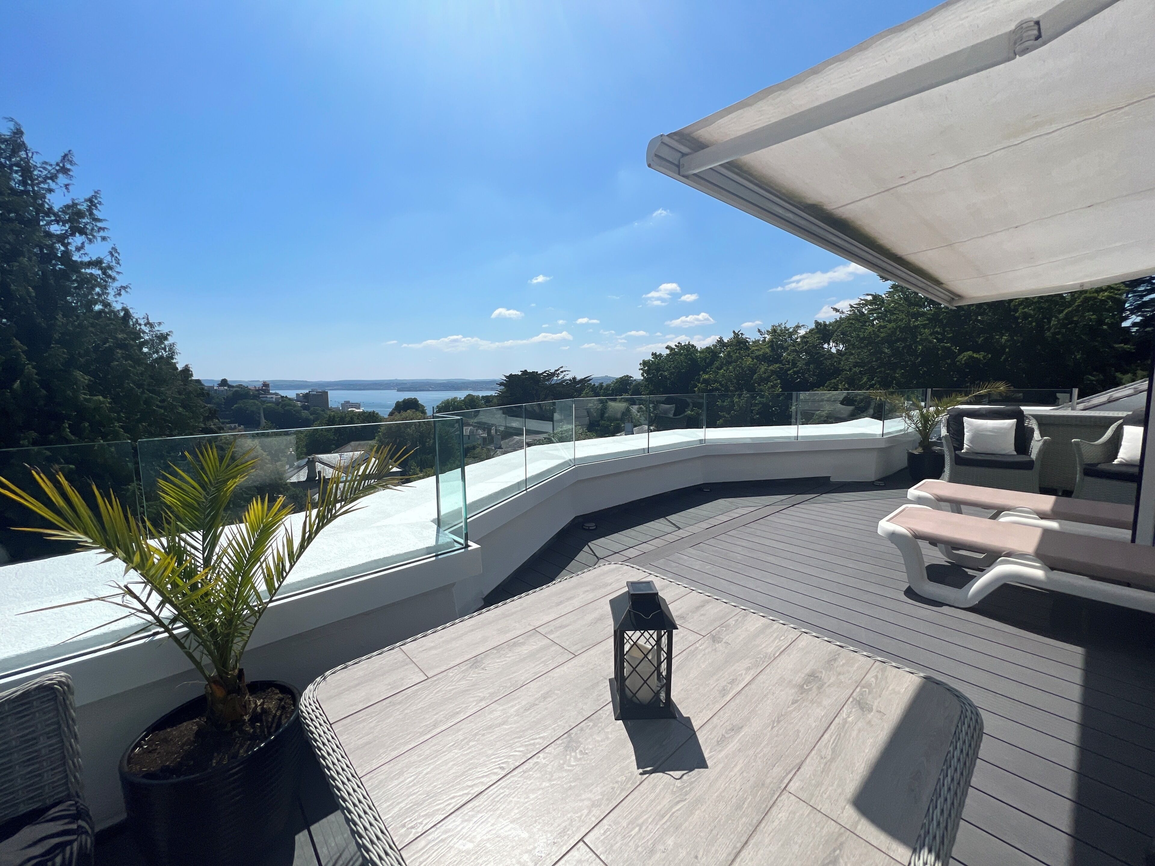 A modern outdoor deck with a curved railing, lounge chairs, and a potted plant.