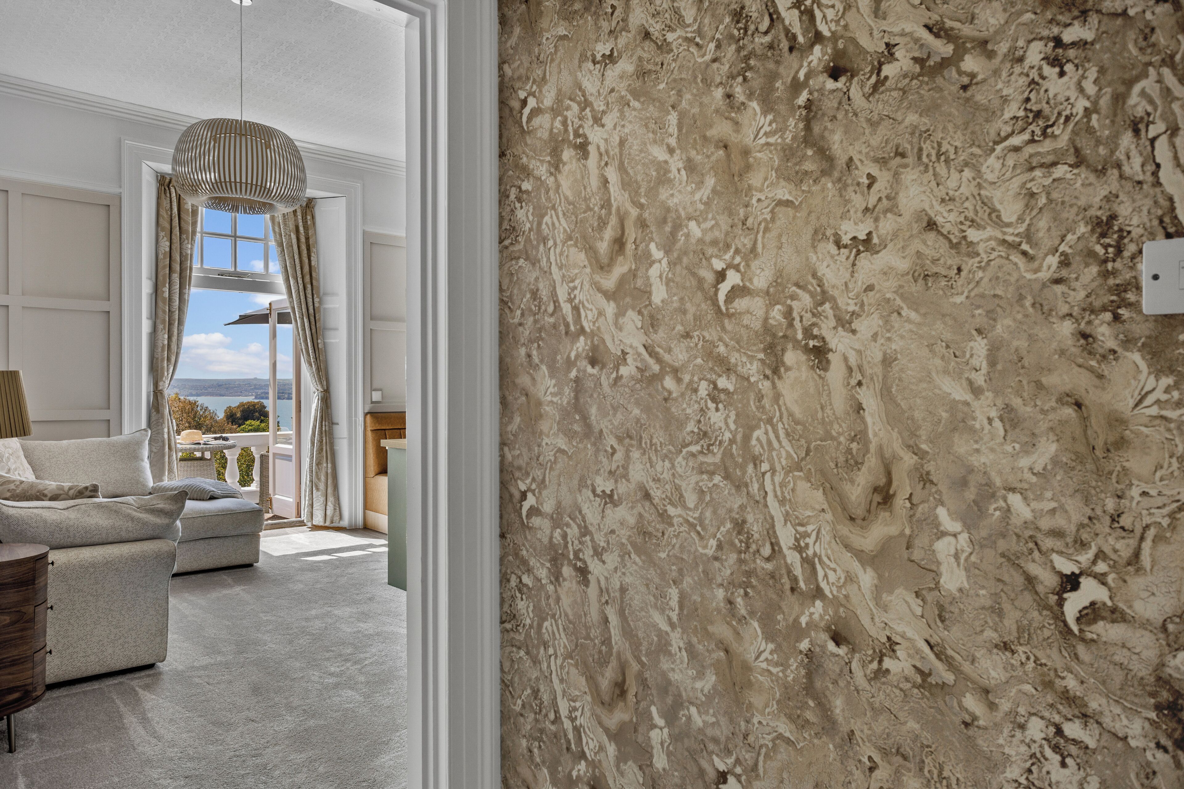 Una habitación con pared de mármol, un sofá, una lámpara colgante y vistas al exterior.